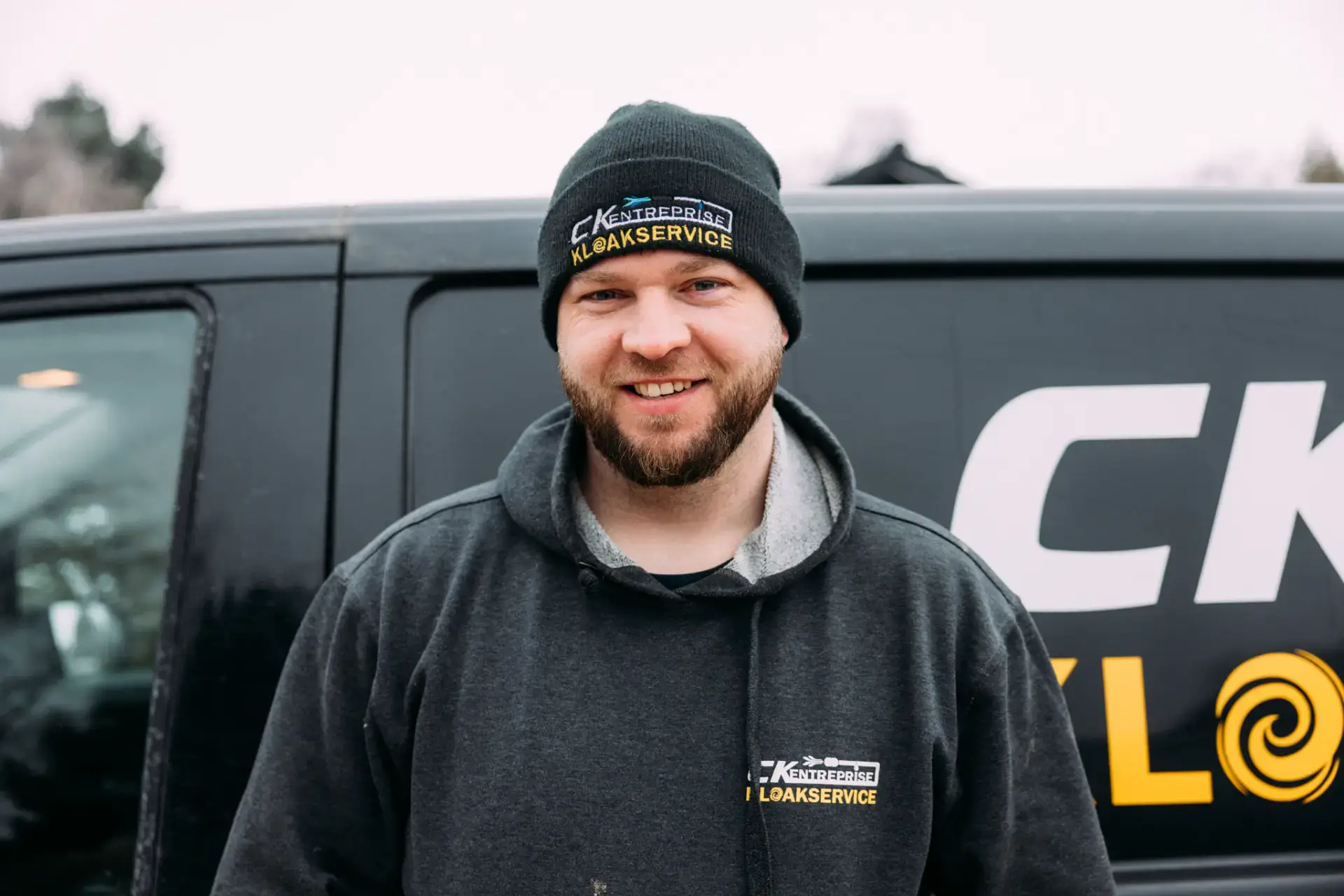 Kloakservice specialist med uniform og servicebil foran firmaets køretøj.