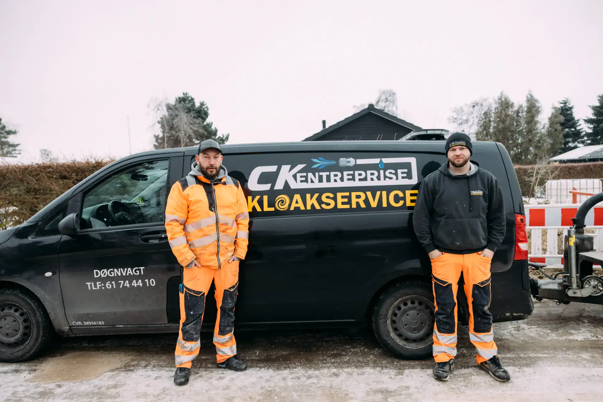 To kloakservicearbejdere står ved en servicebil på byggepladsen.