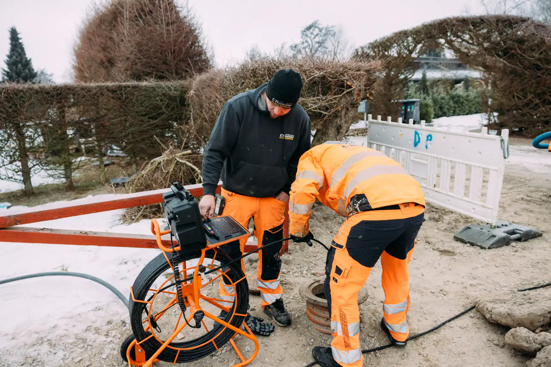 To kloakarbejdere udfører rørinspektion med kameraudstyr i udendørs område.