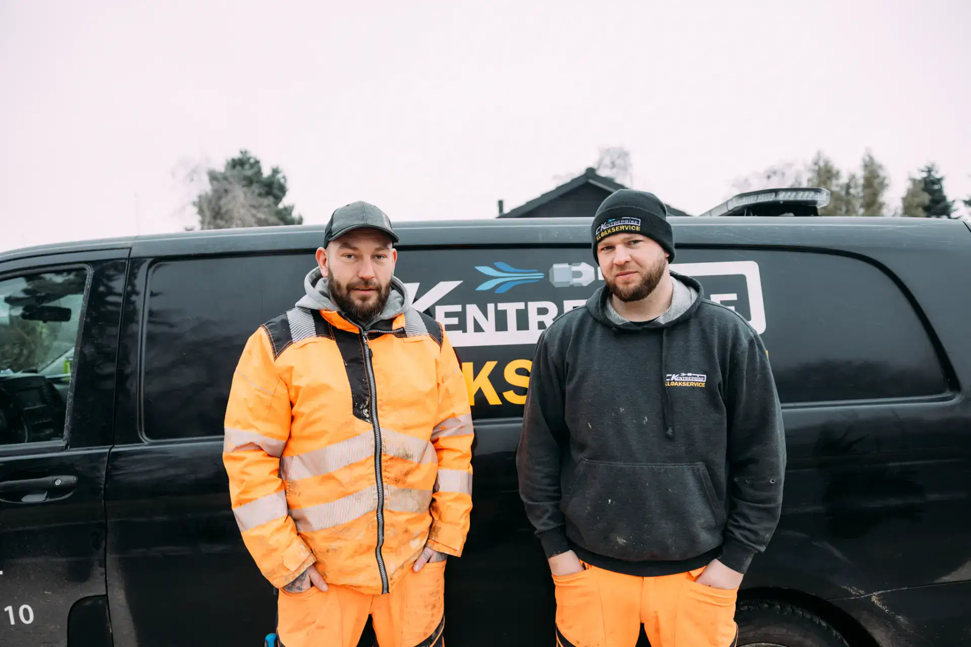 Kloakservice team står foran firmabil med logo, klar til at håndtere kloakproblemer.