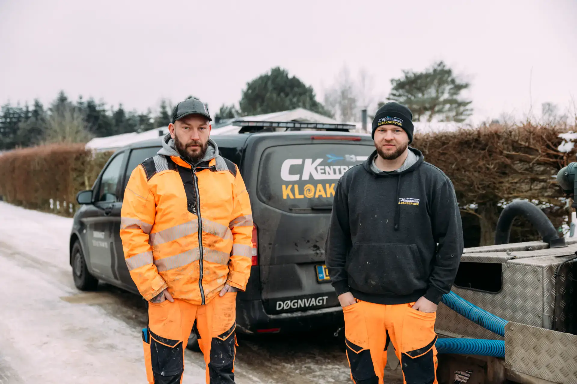 To kloakservicearbejdere står foran en servicebil i vintervejr.