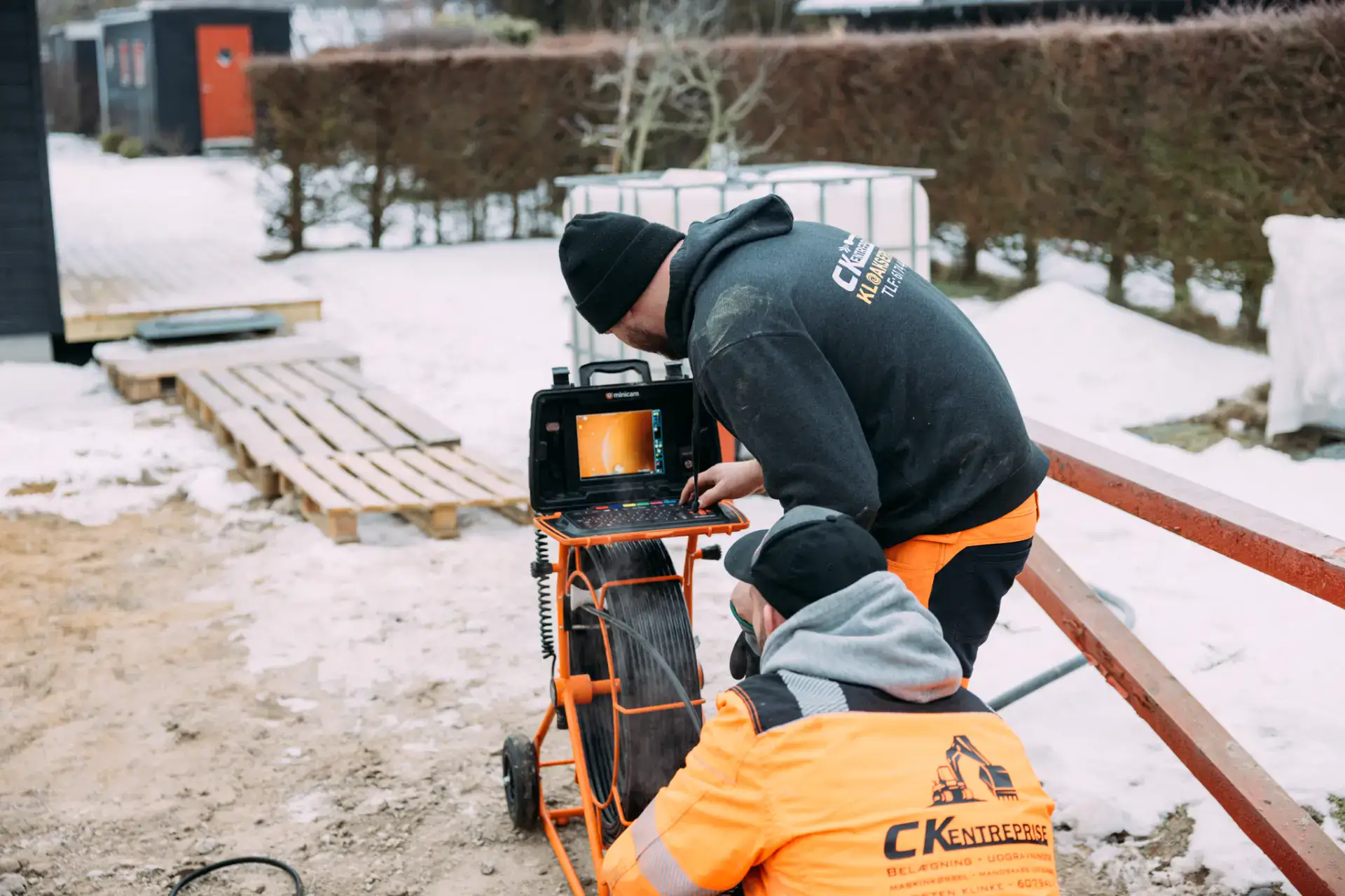 To kloakarbejdere arbejder med inspektion i sneklædt udendørsområde.