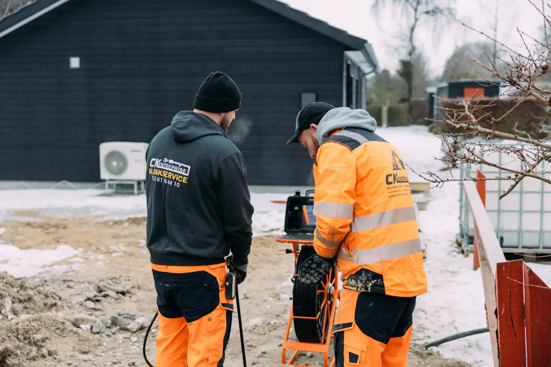 Kloakservice i aktion med to teknikere, der arbejder på udendørs kloaksystem.